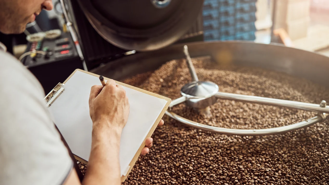 Panama specialty coffee - Close Up Young Man Hand Writing Clipboard While Gentleman Standing By Cooling Tray With Roasted Coffee Beans